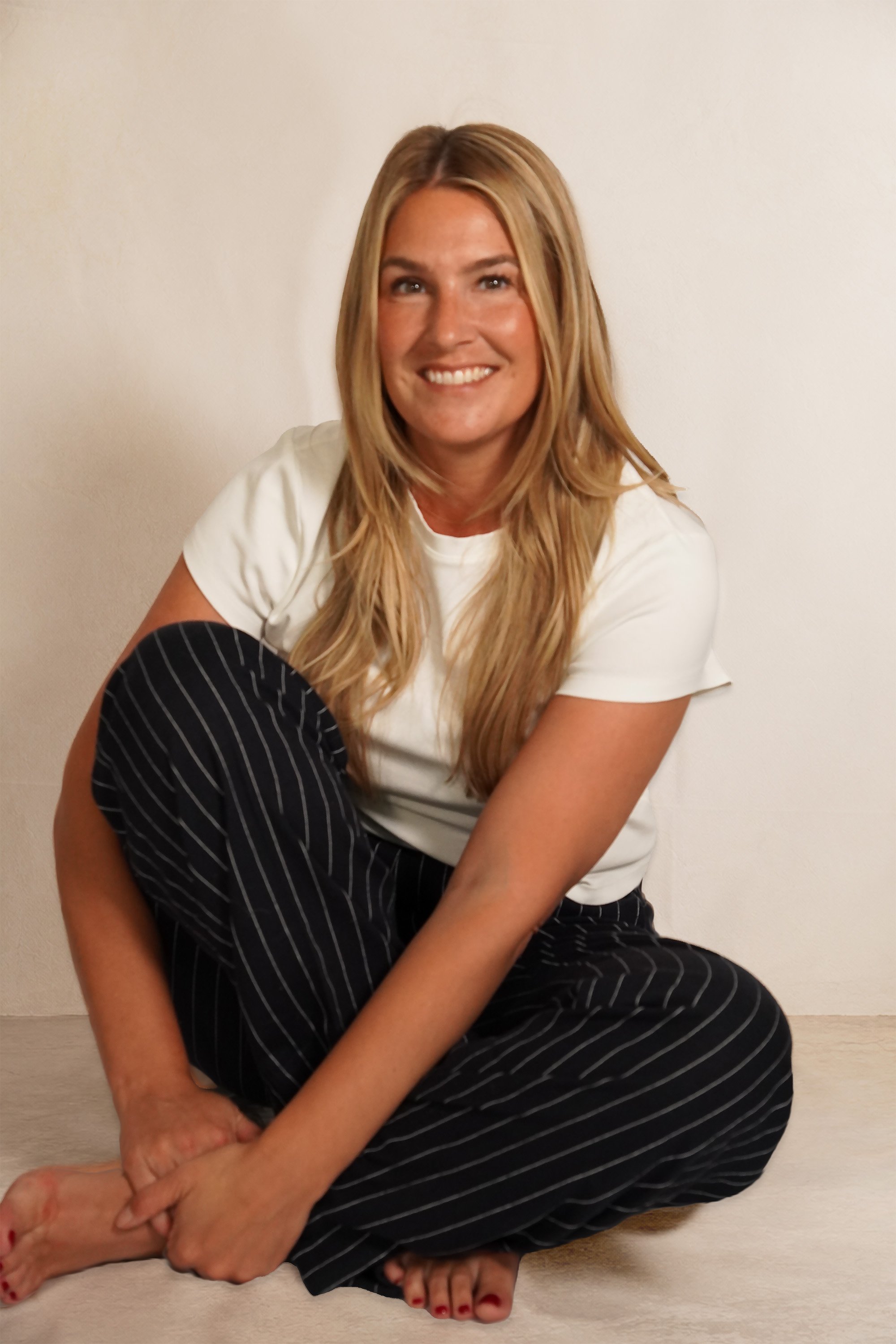 Bonnie smiling, seated on the floor in a white tee and pinstriped trousers